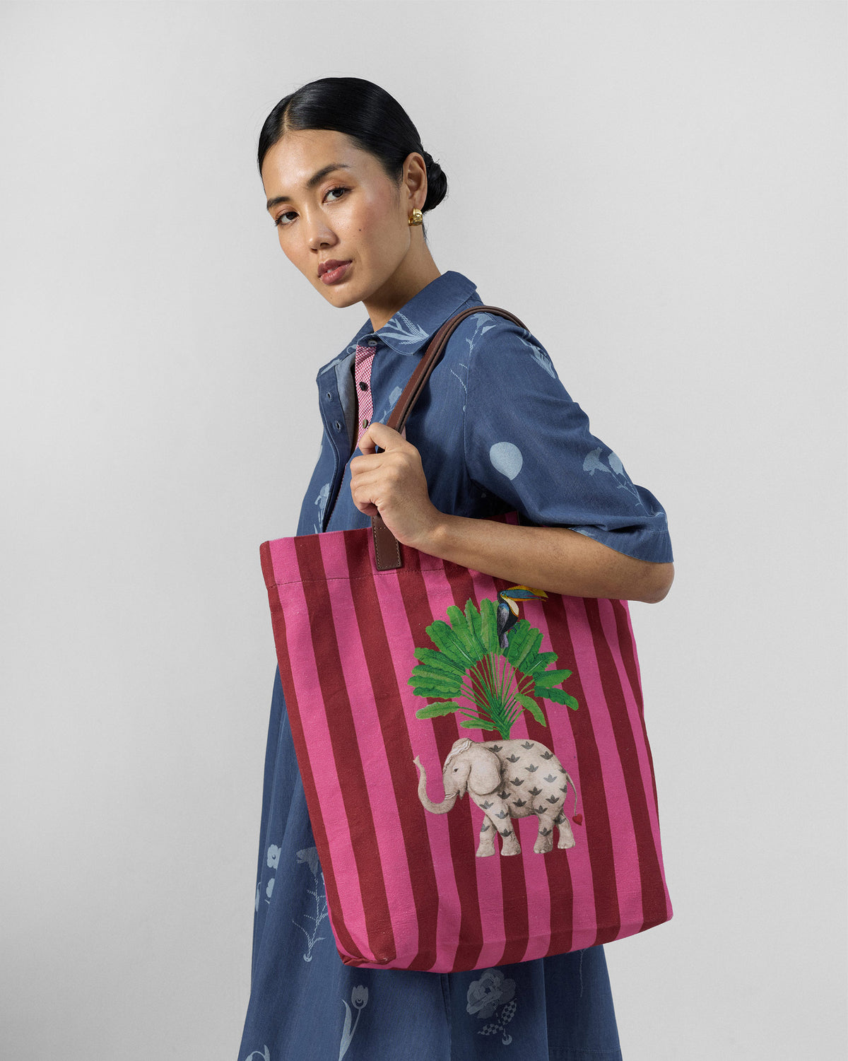 Person carrying a pink and maroon Mukayu city tote with an elephant print.