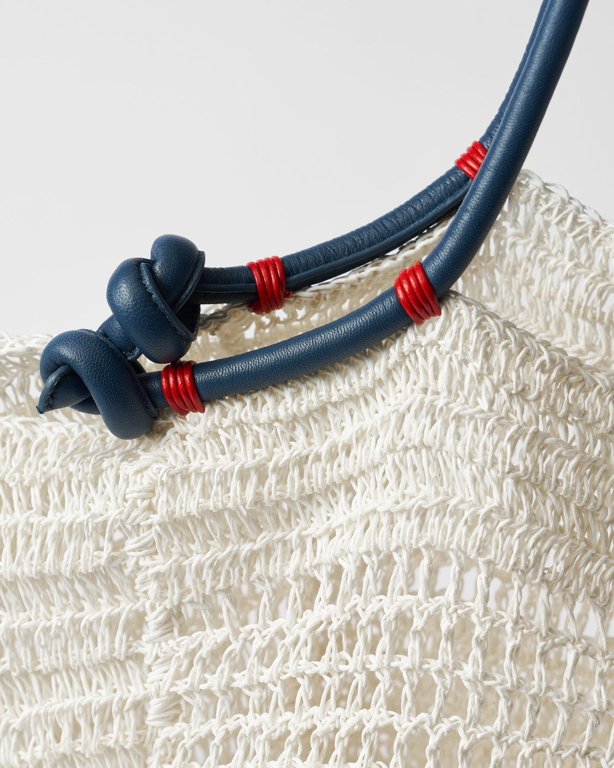 Close-up of navy knotted handles with red wraps on a cream woven bag.