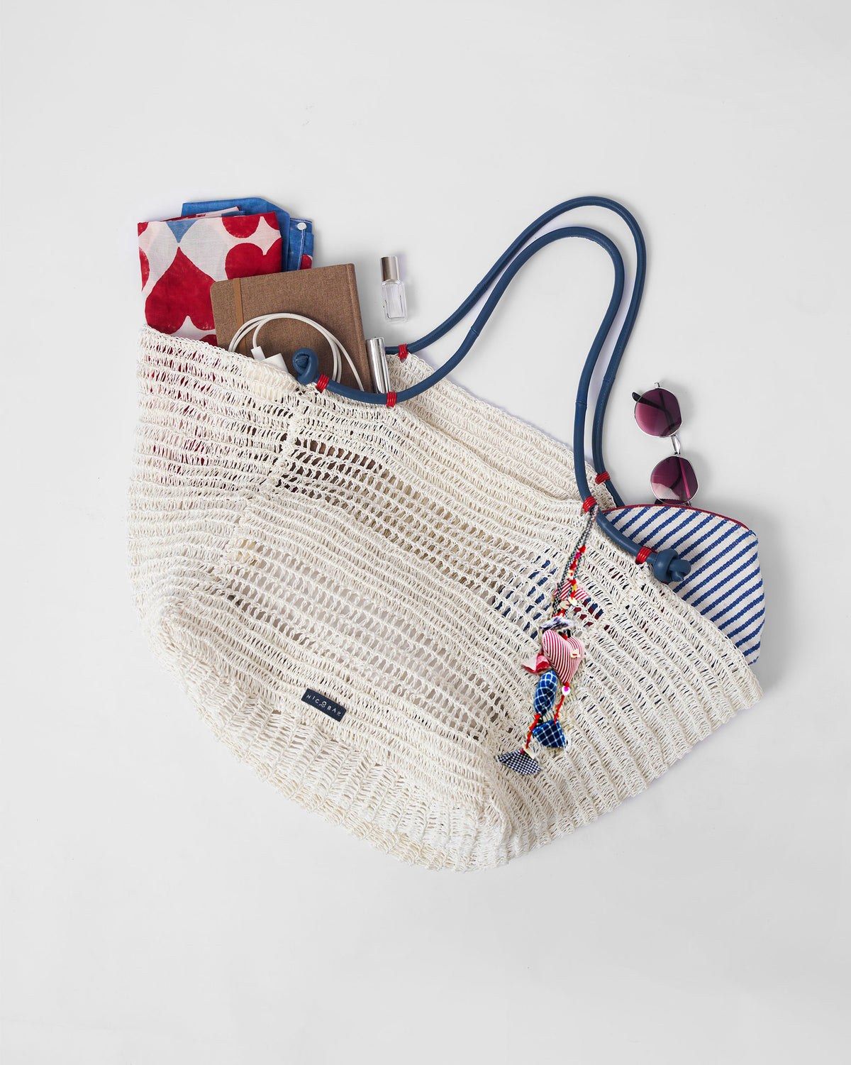 Open cream woven Riya tote packed with everyday essentials and a heart charm.