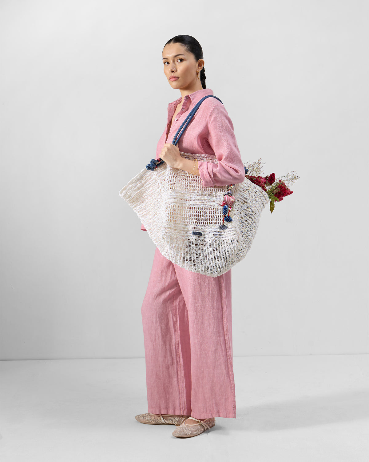 Person carrying a large cream open-weave Riya tote with navy straps.