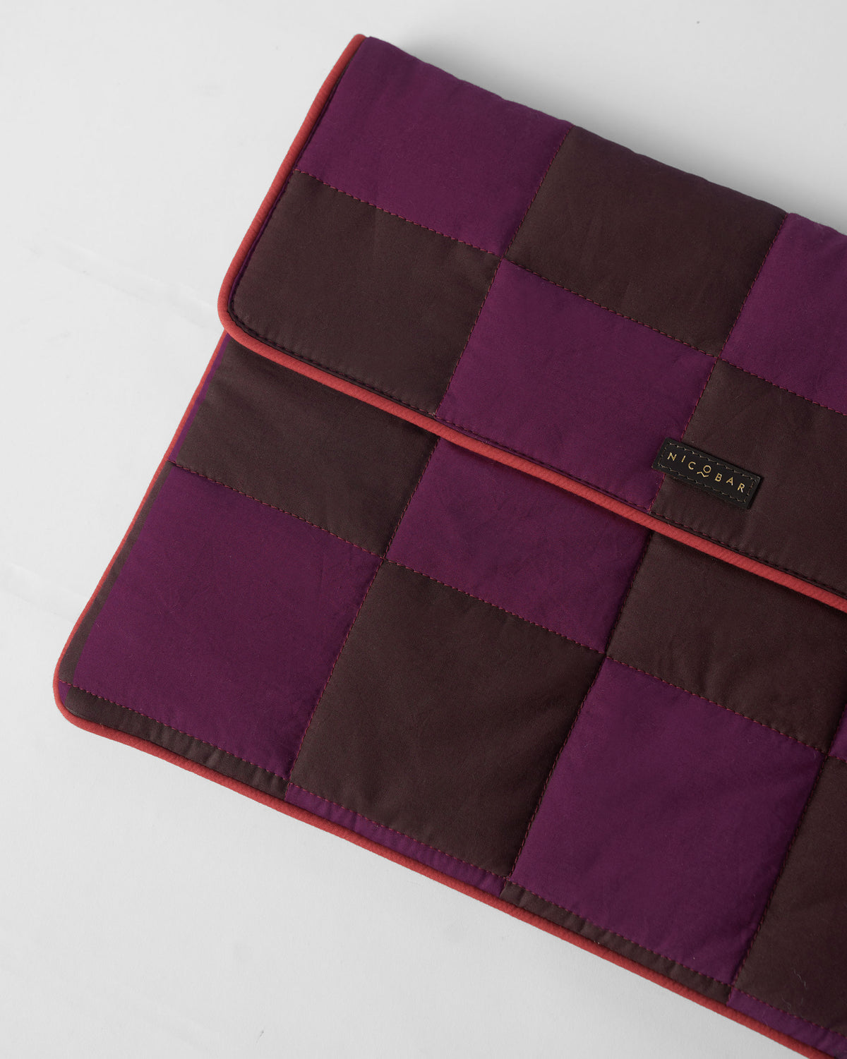 Close-up of a quilted brown and mulberry Tiled Laptop Sleeve with red piping.