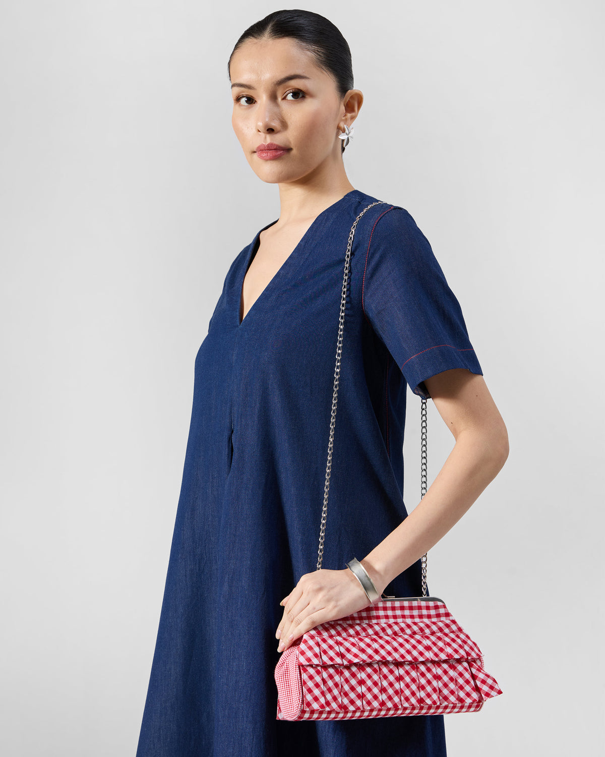 Red and white gingham Pleated Muse Clutch with a silver chain, worn at the hip.
