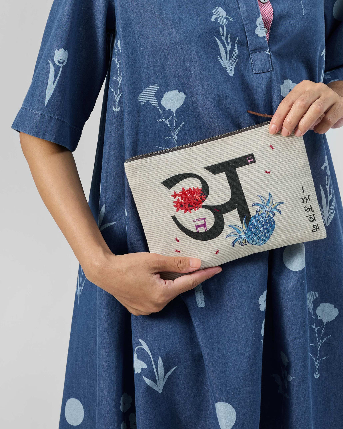 Ivory Anaar Pouch with a black letter motif and pomegranate accents, held in hand.