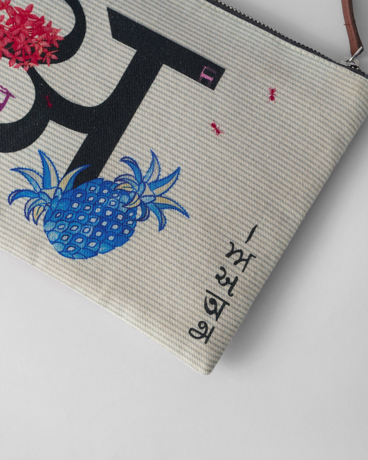 Close-up of the blue pineapple and flower motifs on an ivory Anaar Pouch.