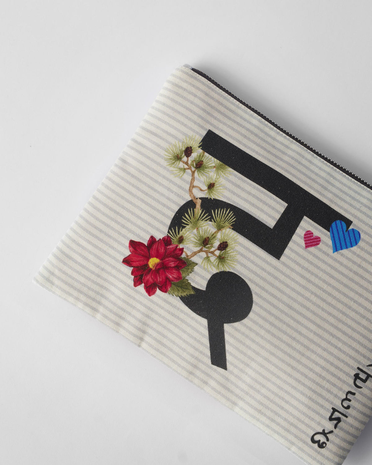 Close-up of the flower embroidery and letter print on an ivory Dil Pouch.