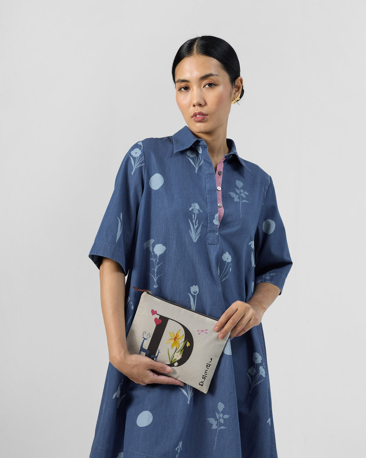 Ivory Dil Pouch with a black D print, held in front of a blue dress.