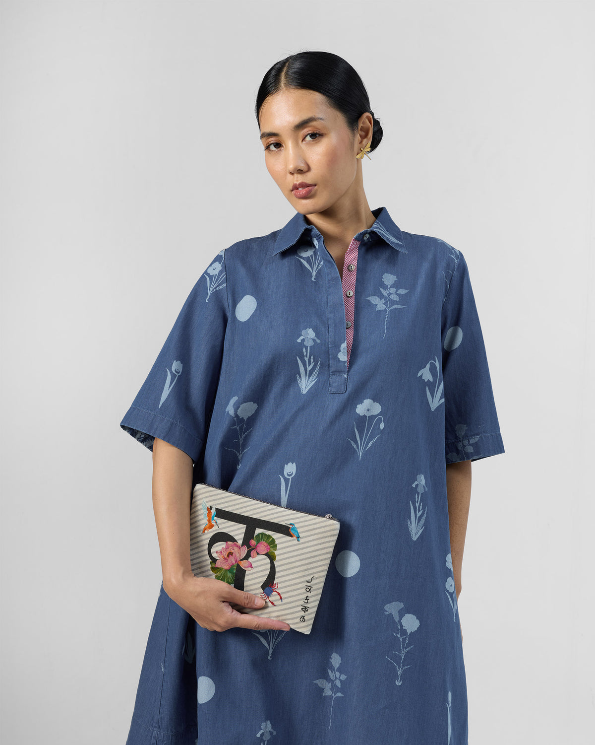 Ivory Kamal Pouch with a lotus and bird print, held in front of a blue dress.