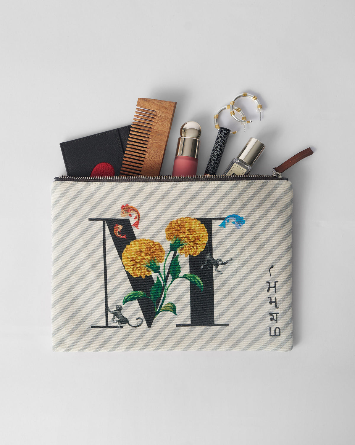 Open ivory Machli Pouch packed with a comb, bottle, and small essentials.
