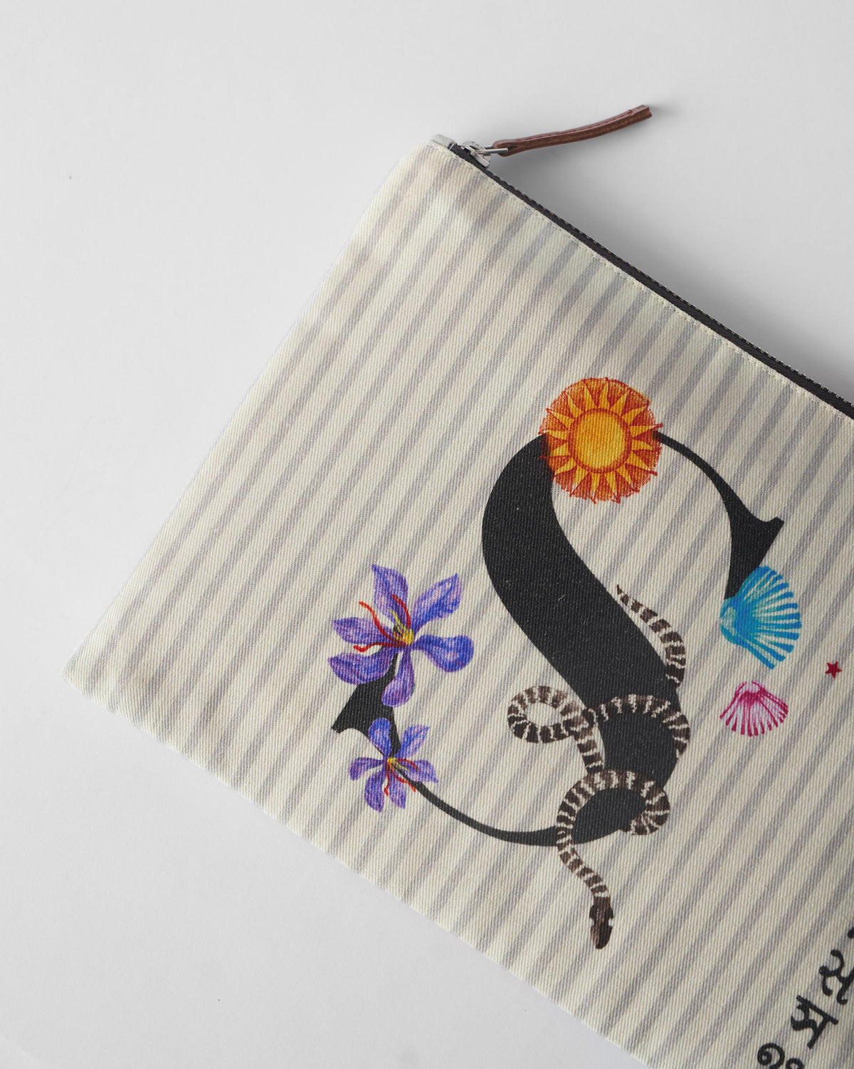 Ivory Sitara Pouch angled to show a black letter S with sun and flower motifs.