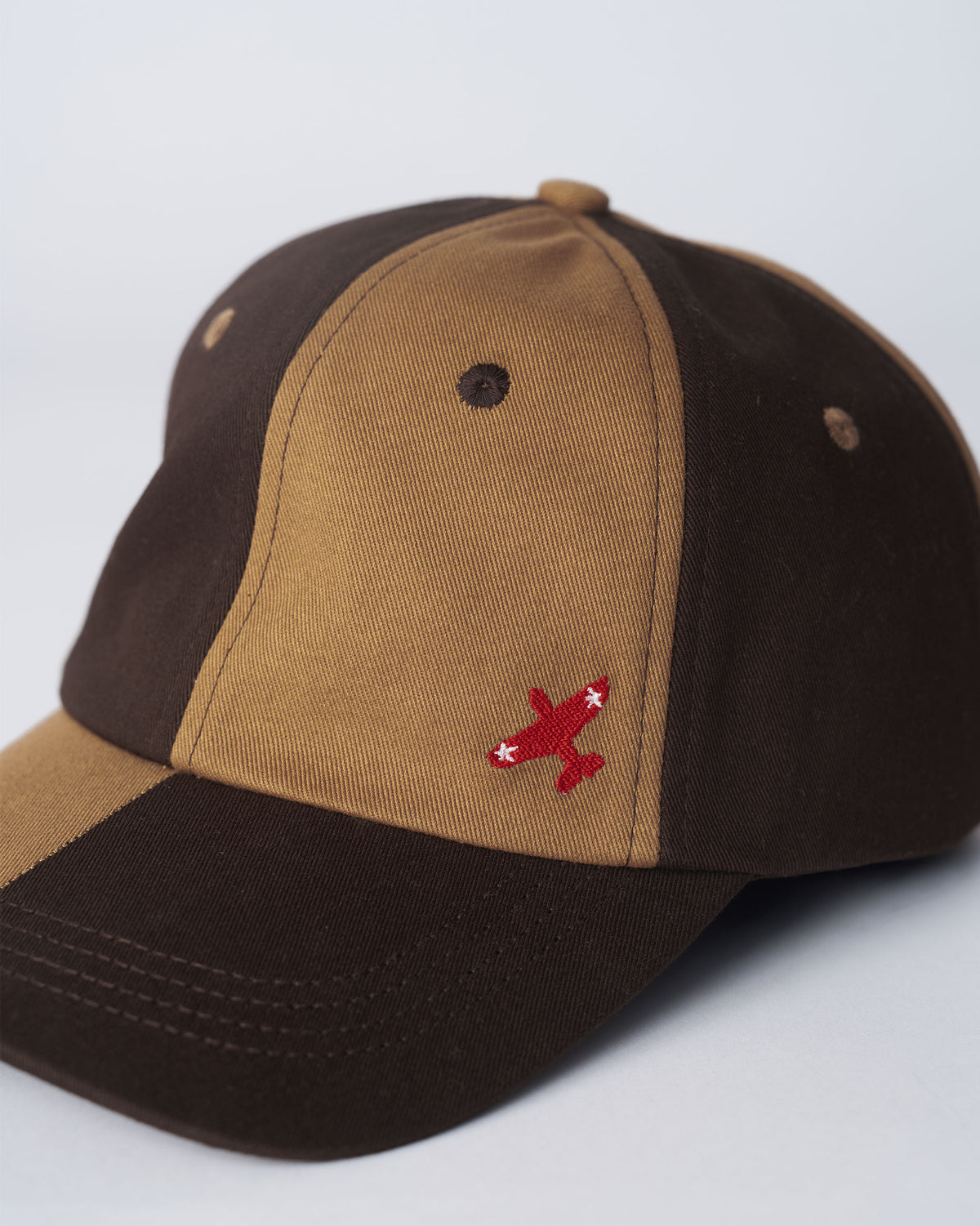 Close-up of the red airplane embroidery on a brown and beige Aero Cap.