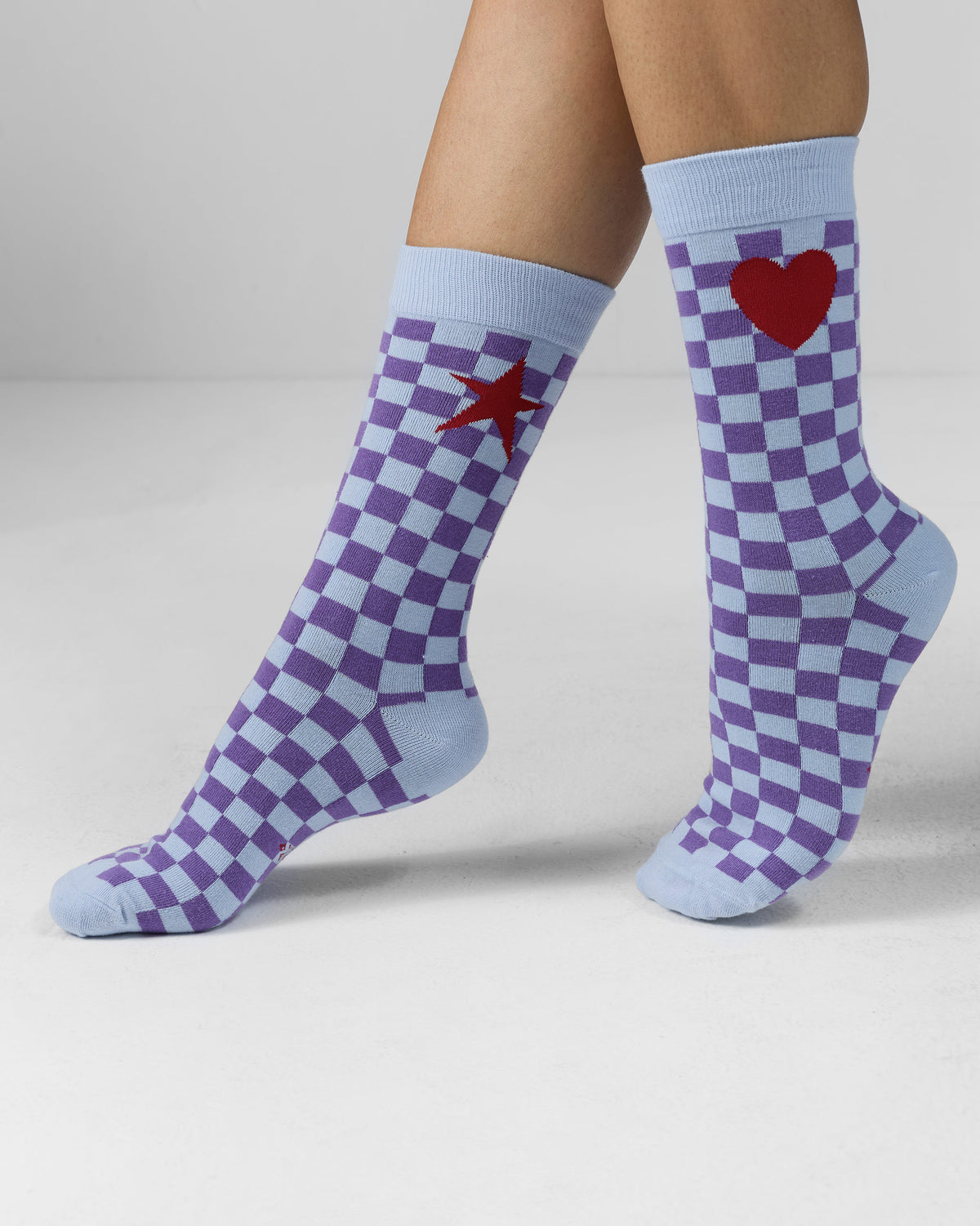 Person wearing ice blue and purple Gingham Glow Socks with a heart and star.