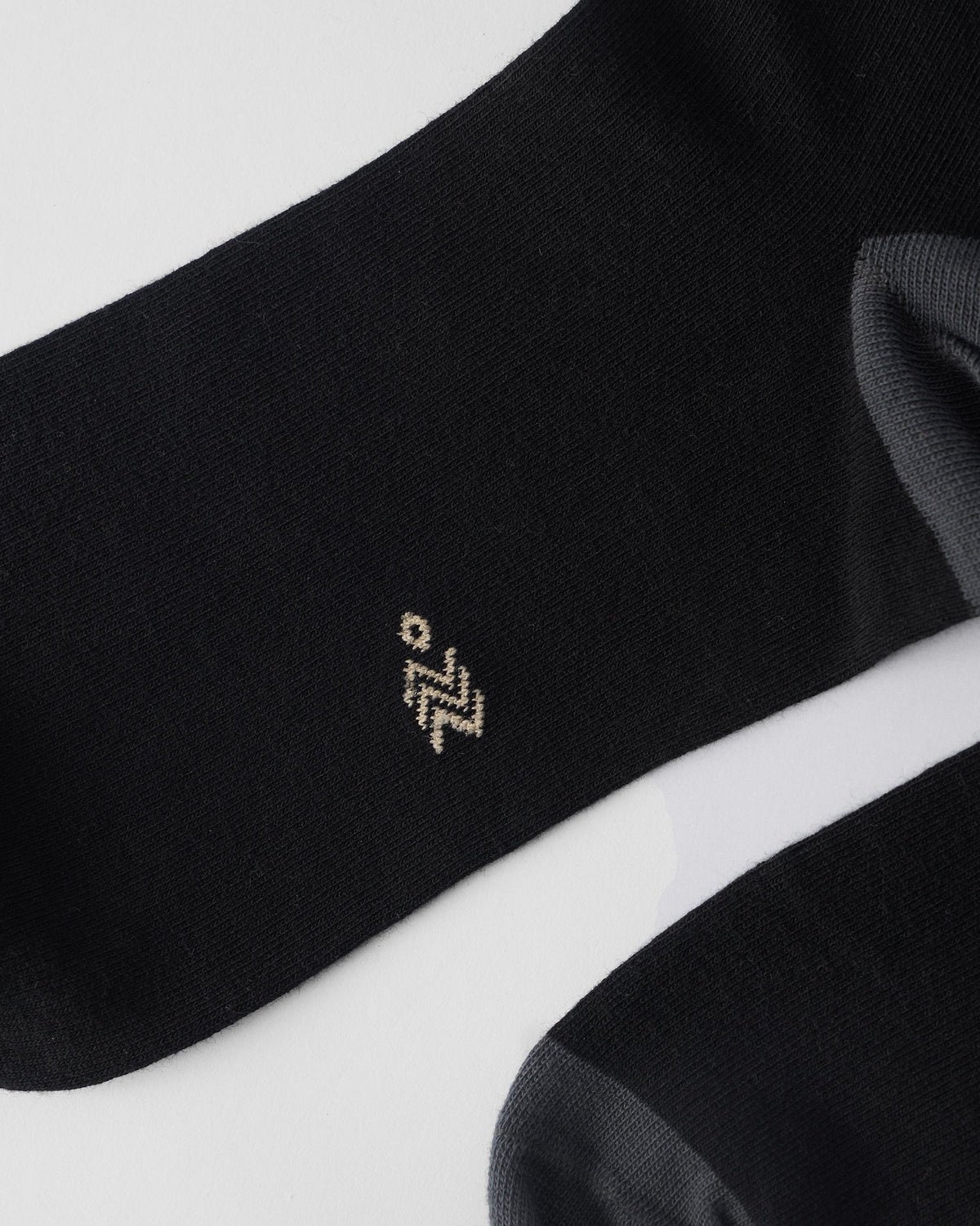 Close-up of a black sock showing the tan Nicobar logo near the heel.