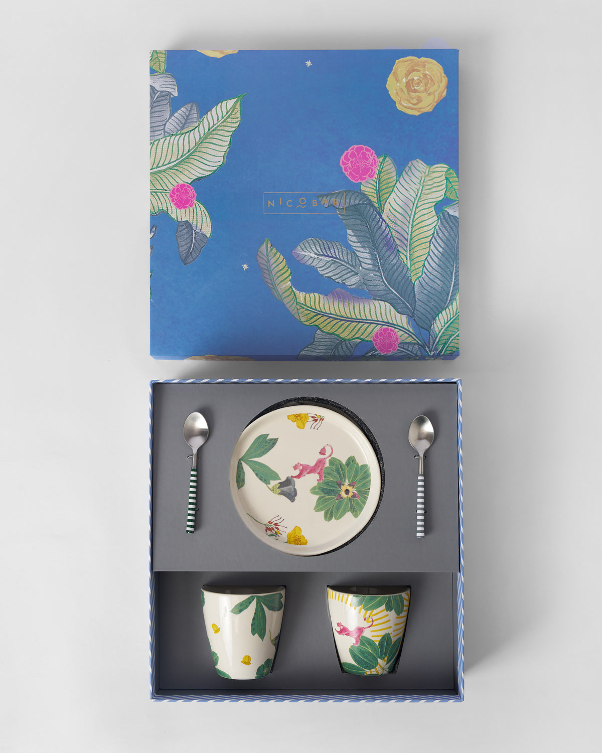 Open Waadi gift box with dessert plate, two mugs, and striped spoons nestled inside.