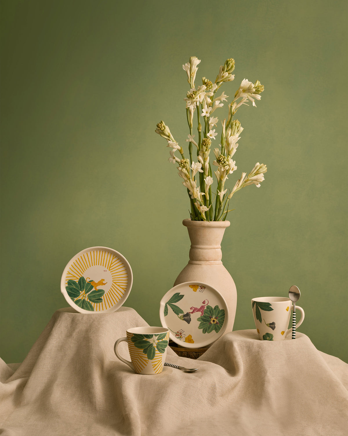 Waadi mugs and dessert plates styled on linen with a vase of white flowers.