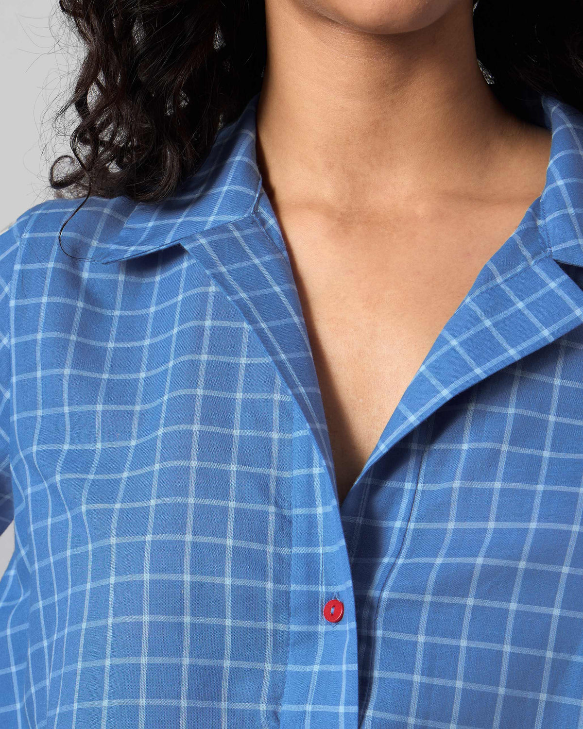 Close-up of a red button on a riverside blue checked Rann shirt.