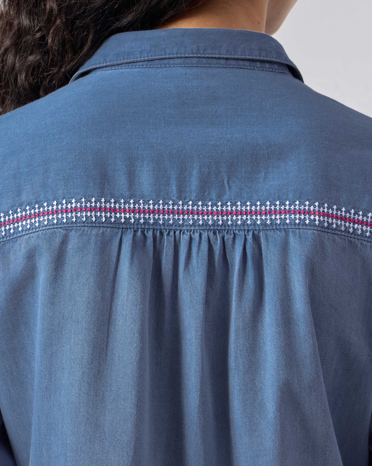Close-up of pink cross-stitch on a blue Pristine dress yoke.