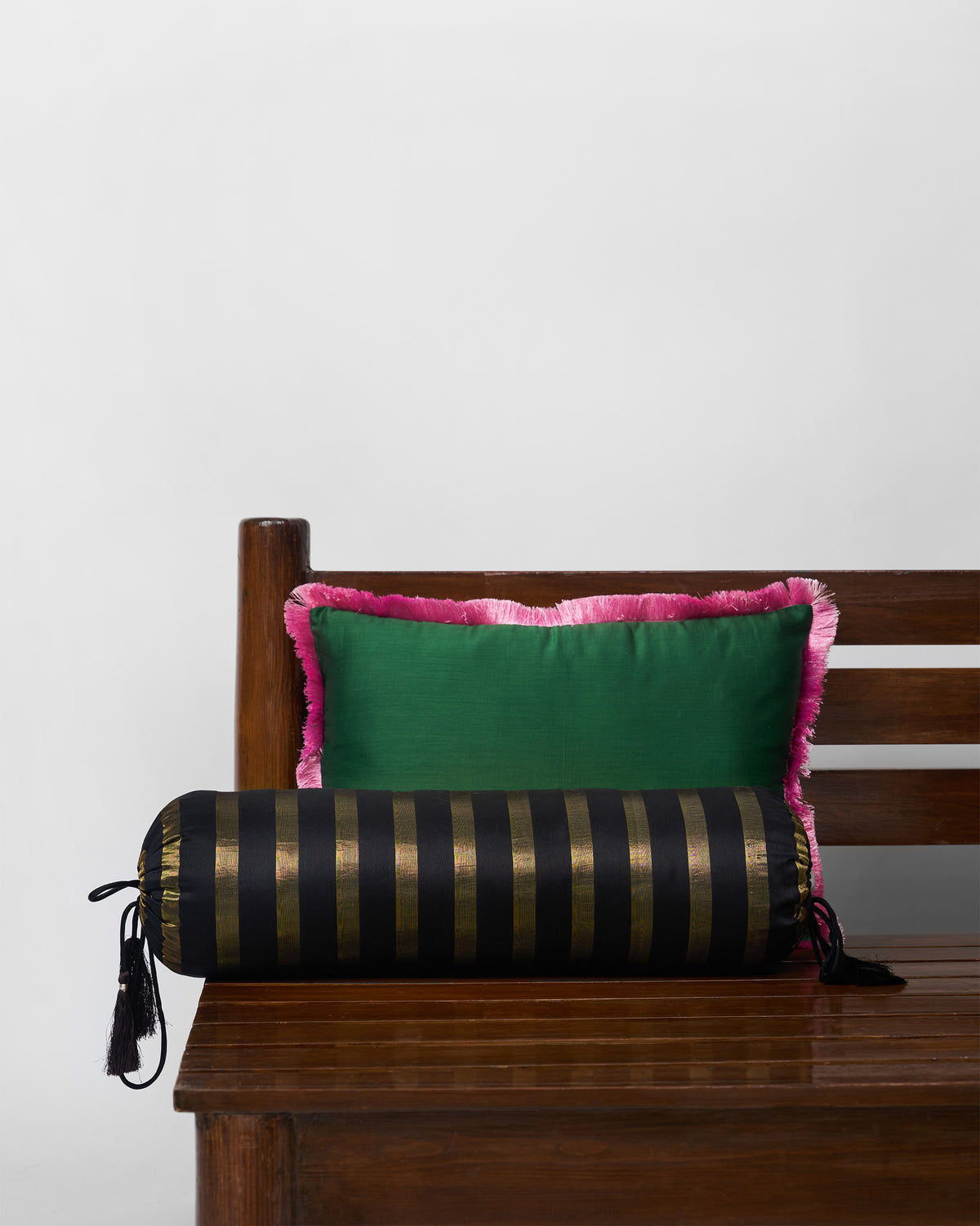 Tassel Bolster Cover in black and gold stripes with tassels, beside a green fringed cushion.