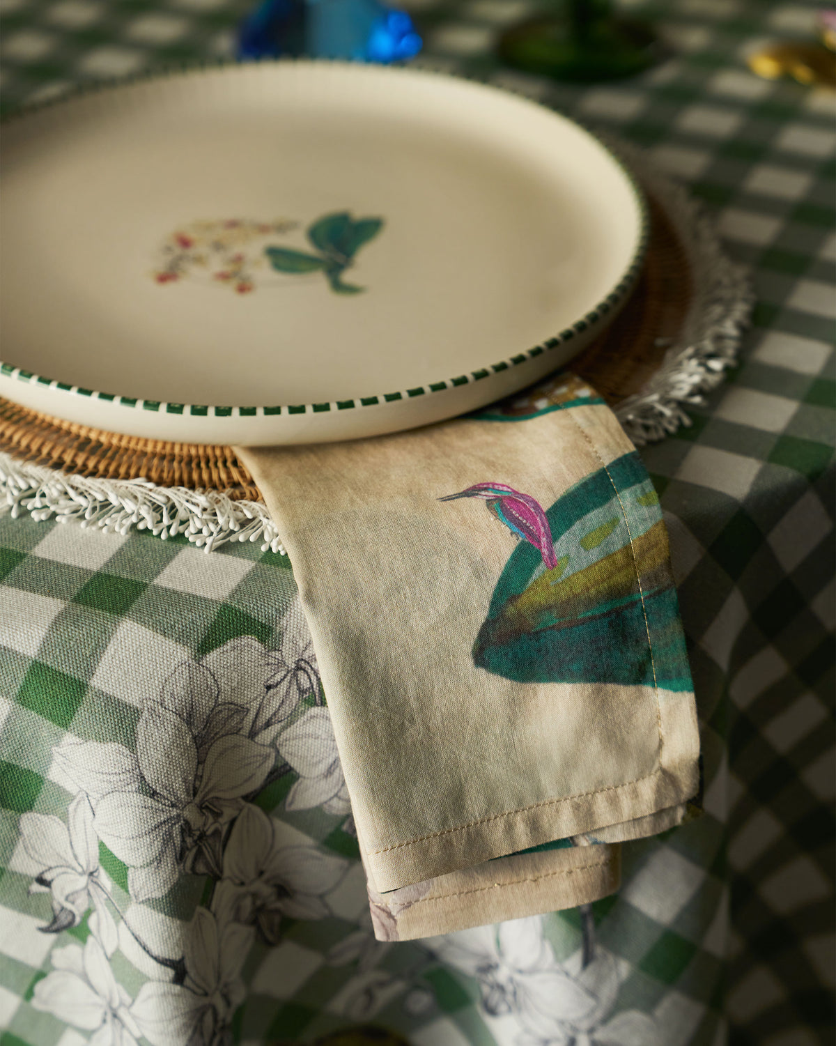 Madhu Napkin with a pink and blue bird print, folded beside a plate.