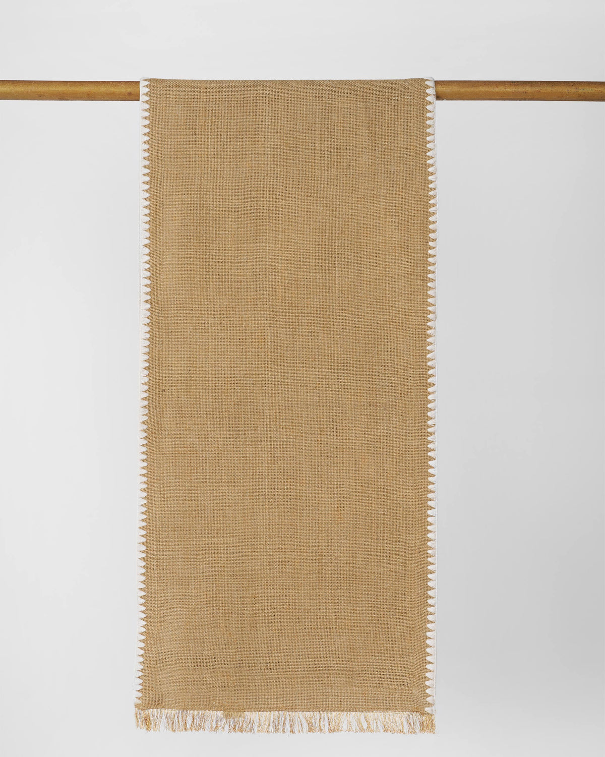 Kaveri Runner in tan with white scalloped edges, hung over a wooden rod.