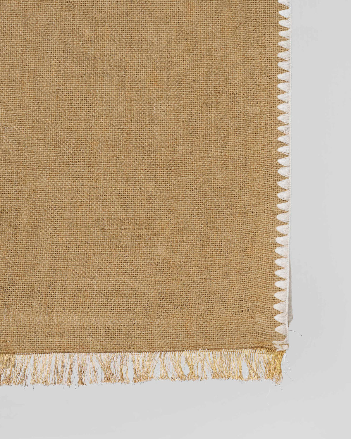 Close-up of Kaveri Runner corner in tan with a white stitched edge and fringe.
