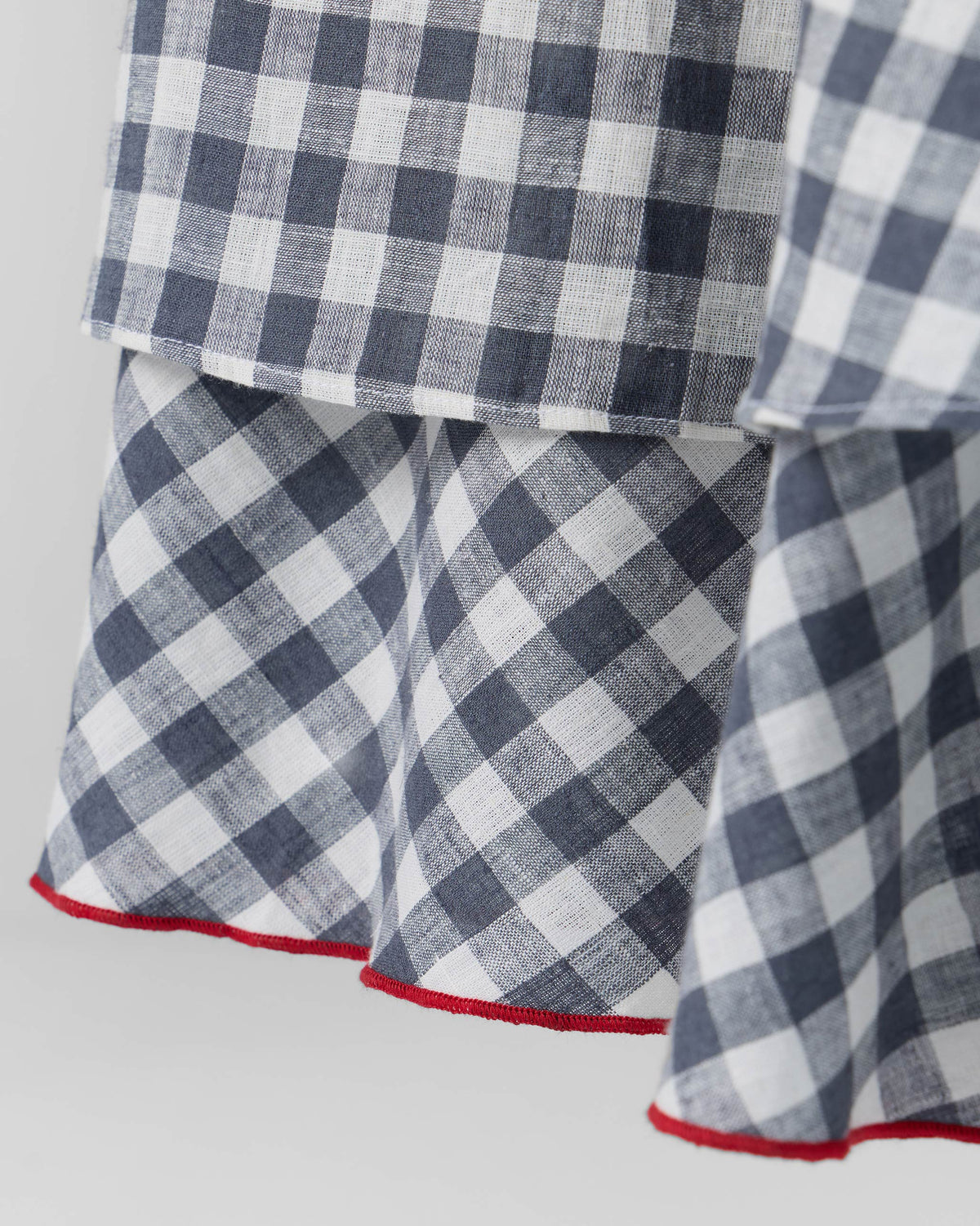 Close-up of the red-trimmed hem on a grey and white check Ezra dress.