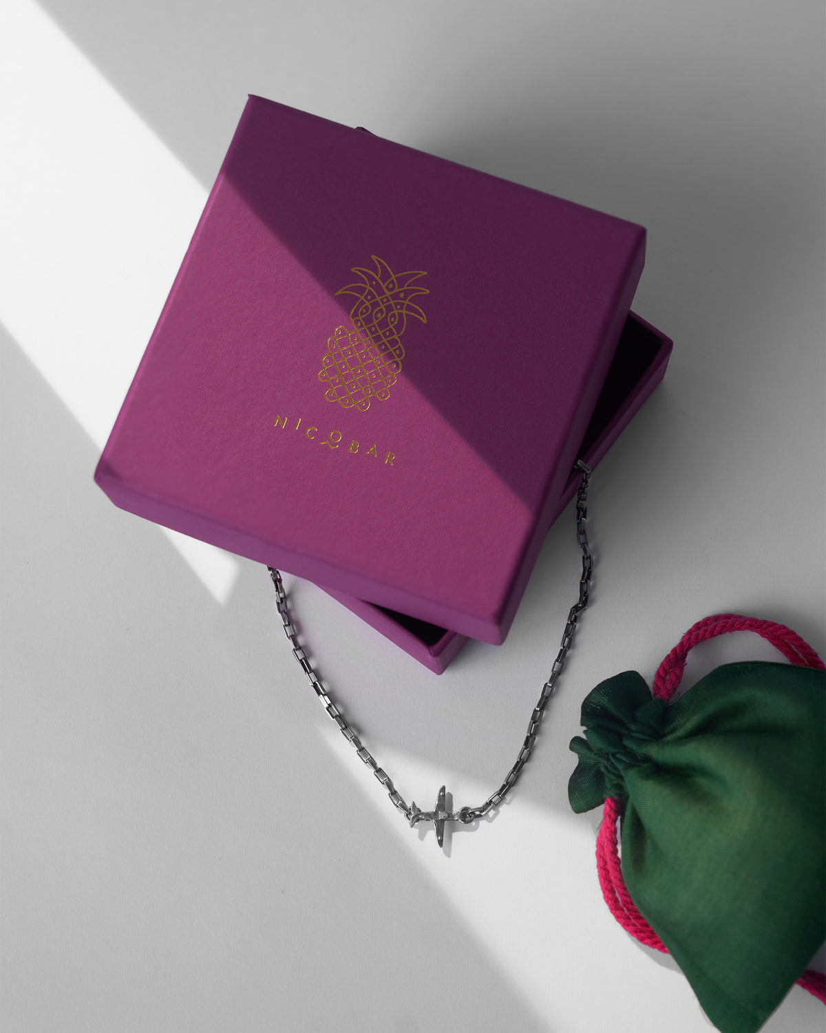 Silver Flight Chain with airplane charm on a magenta Nicobar box.
