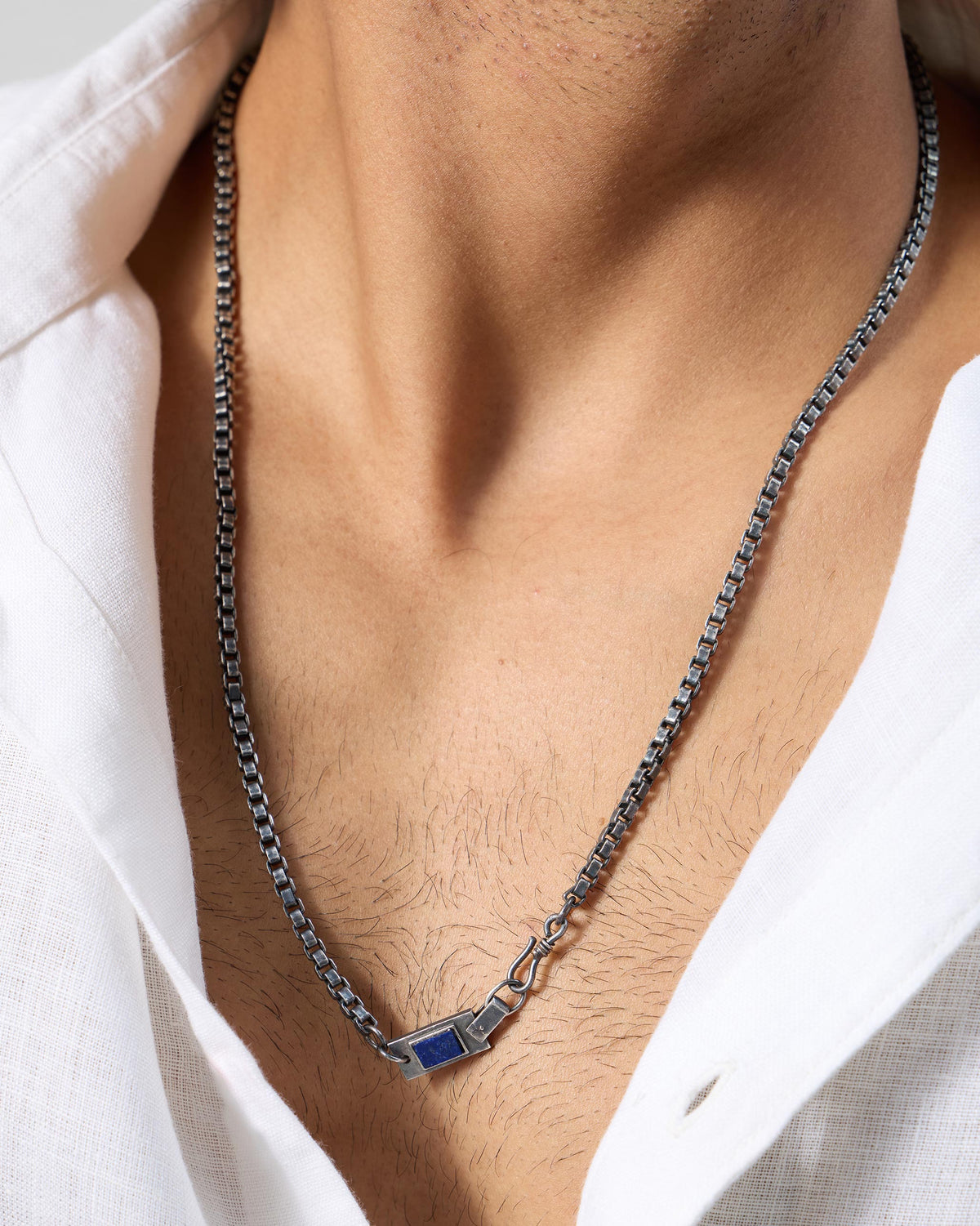 Silver Taro chain with a rectangular lapis accent worn at an open collar.