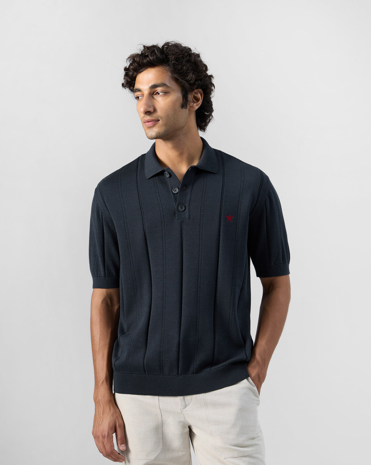 Person wearing a dark navy Midnight polo with a ribbed knit and red chest star.