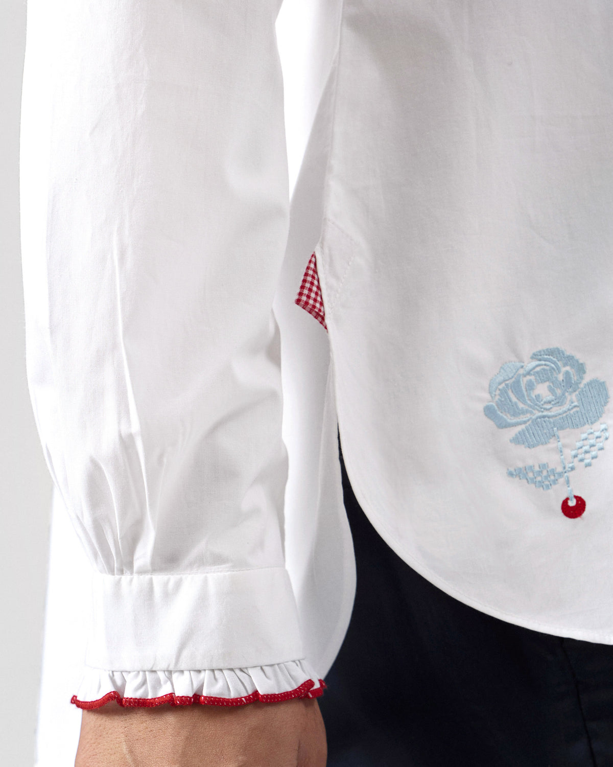 Close-up of a white Sora ruffle shirt showing floral embroidery at the hem.
