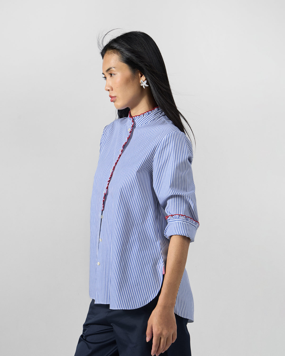 Side view of a blue and white striped Sora ruffle shirt with red trim.