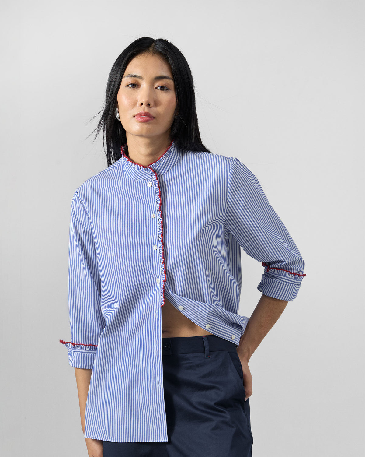 Person wearing a blue and white striped Sora ruffle shirt with red trim.