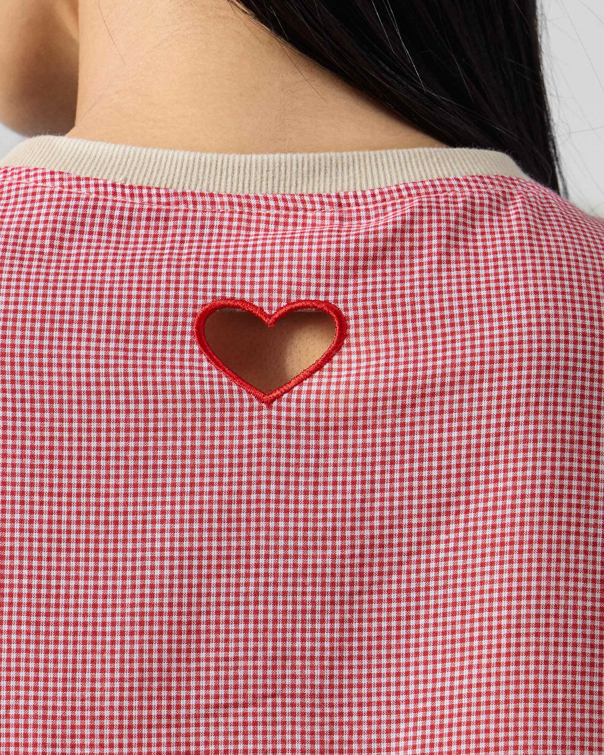 Close-up of a red heart cutwork on the pink checked back of a top.