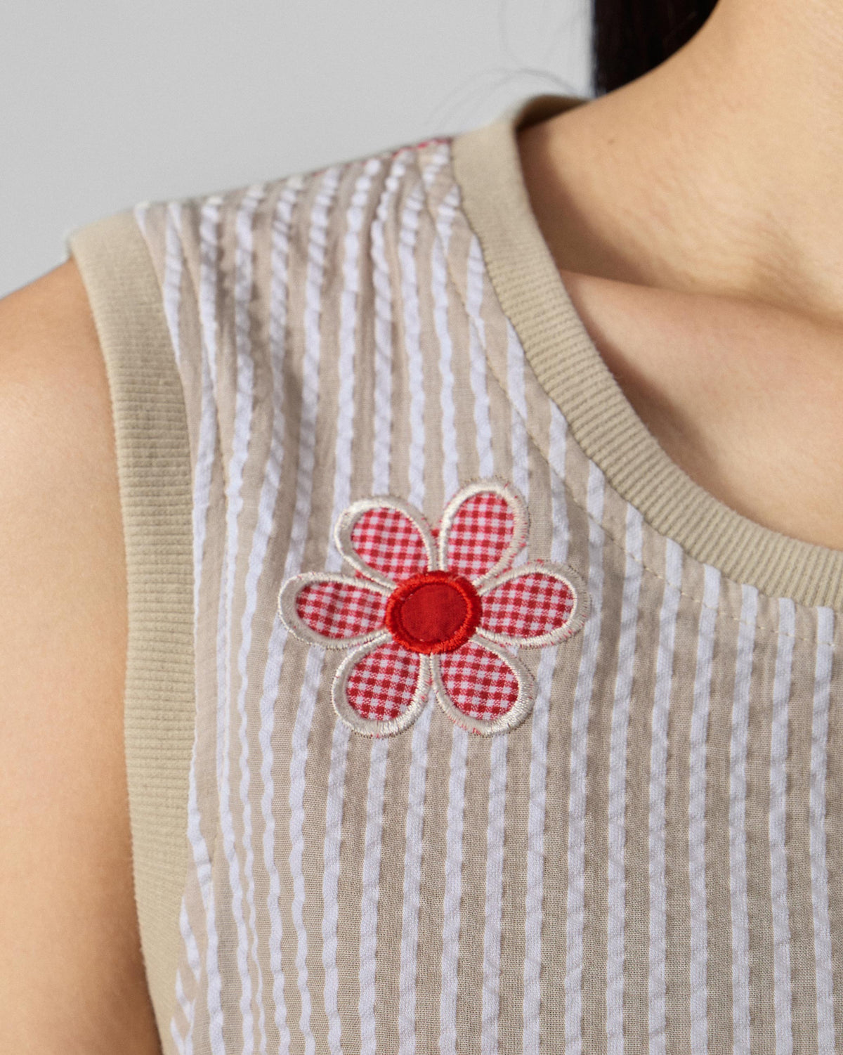 Close-up of a gingham flower appliqué on a brown and ivory seersucker top.