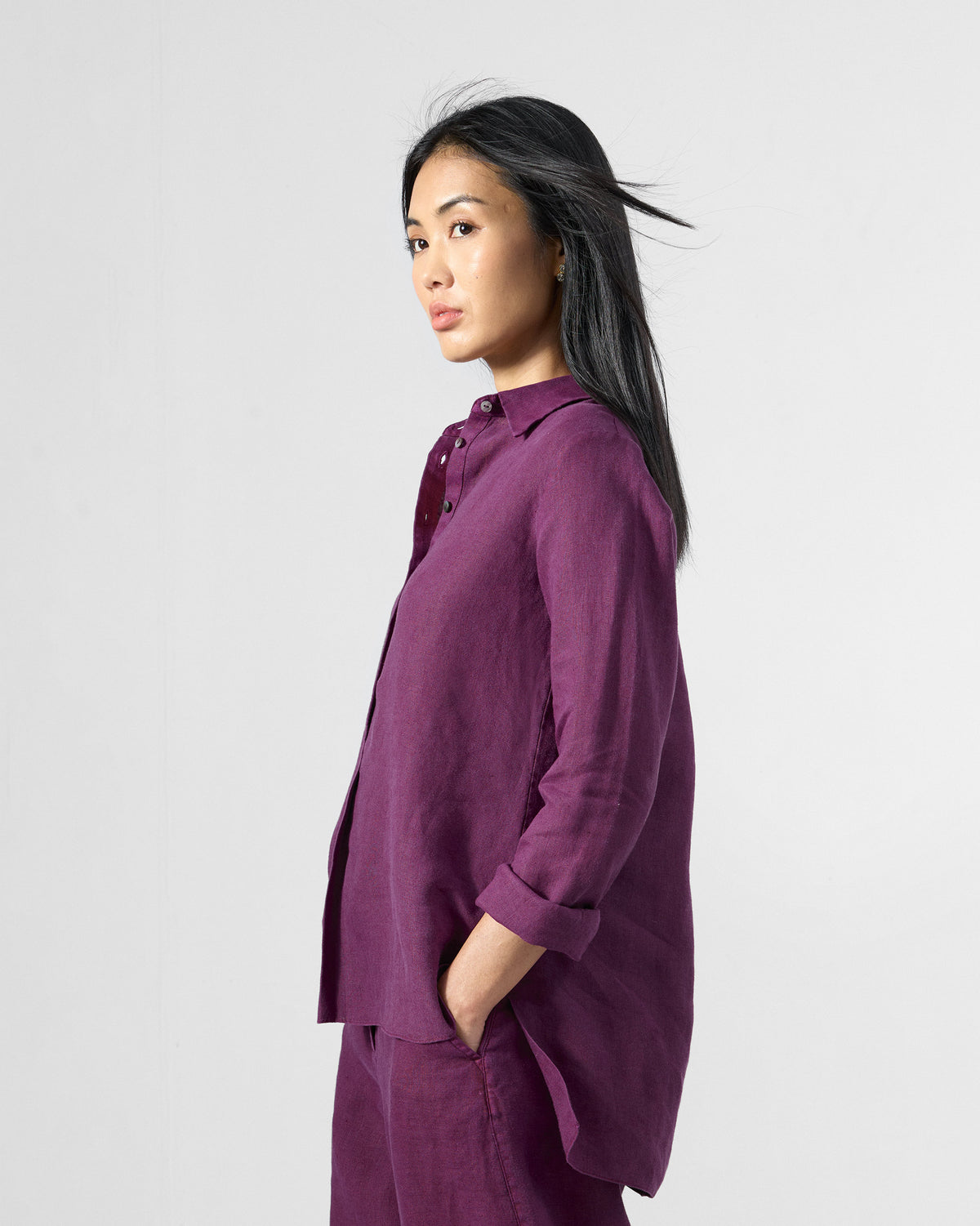 Side view of a plum Mati linen shirt with a curved high-low hem.