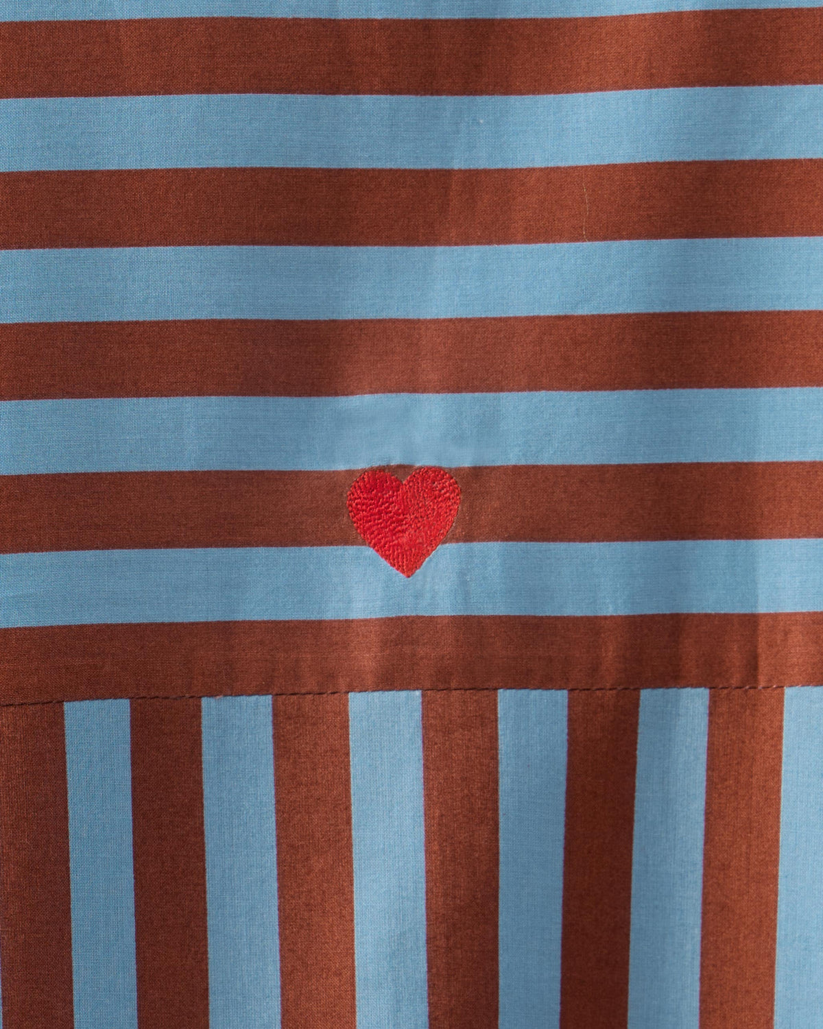 Close-up of a red heart on blue and brown striped Summer Tea dress fabric.