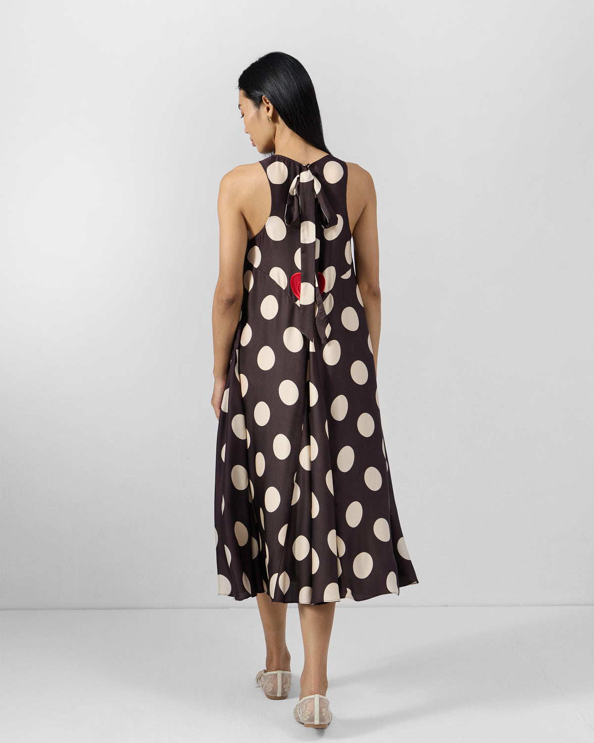 Back of a brown Kinaar Dress with ivory polka dots and a red heart embroidery.