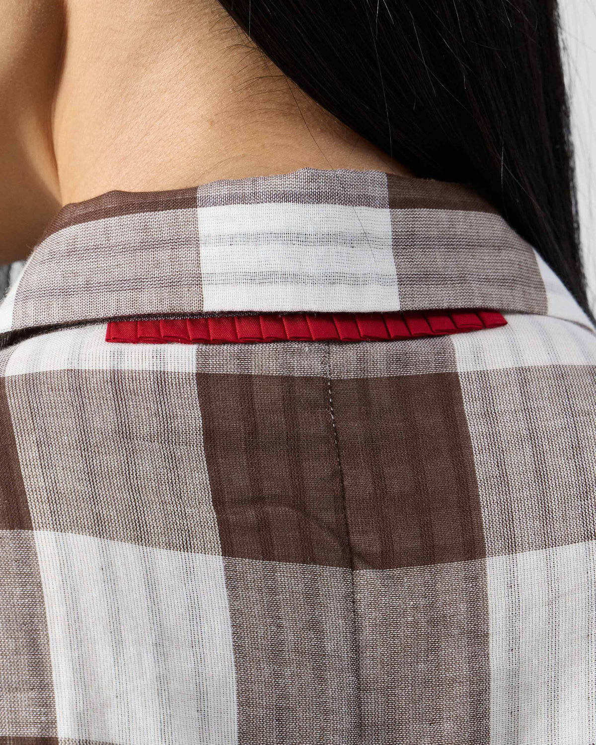Close-up of red ribbon trim at the back neck of the brown and ivory check jumpsuit.