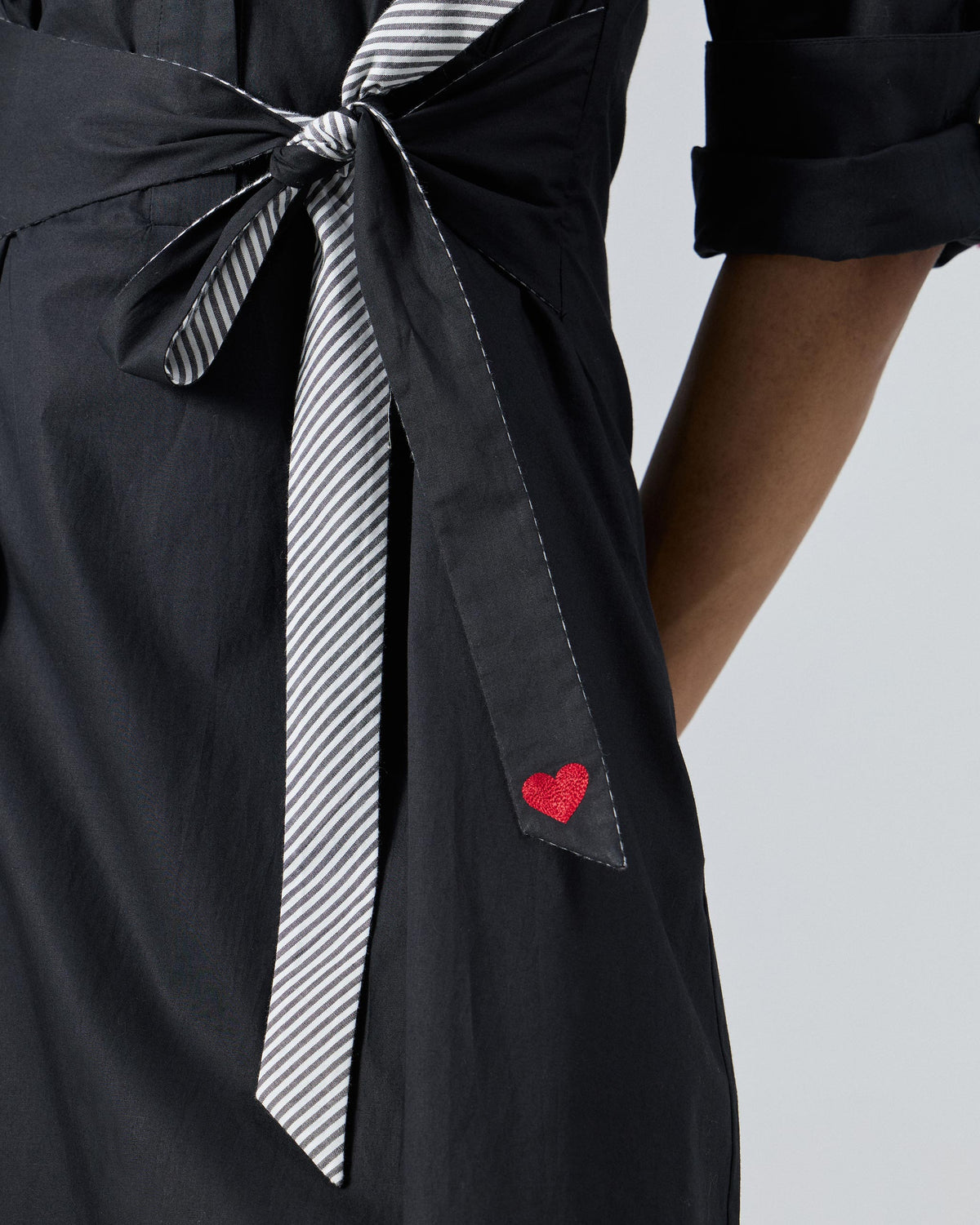 Close-up of a black dress waist tie with a red embroidered heart.