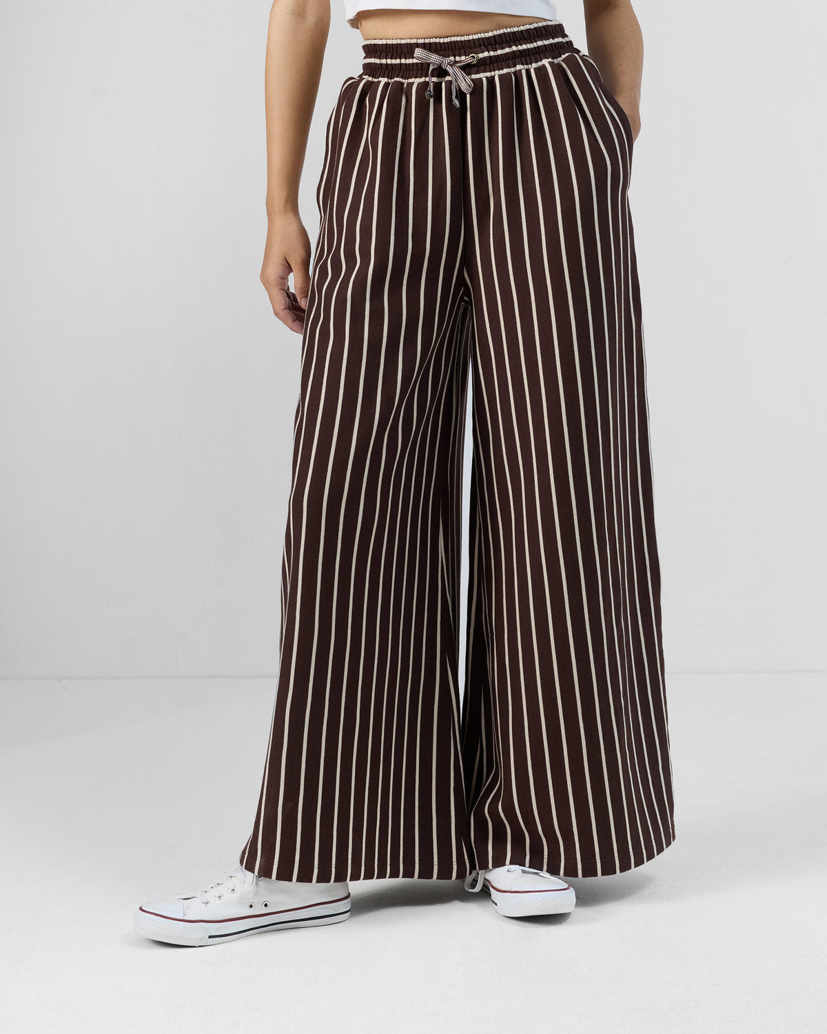 Person wearing brown and ivory pinstripe Nova pants with a drawstring waist and wide legs.