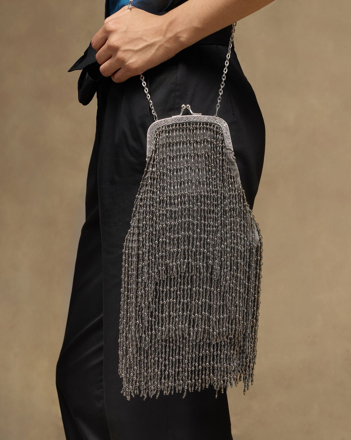 Silver beaded fringe clutch hanging from a chain strap at the hip.