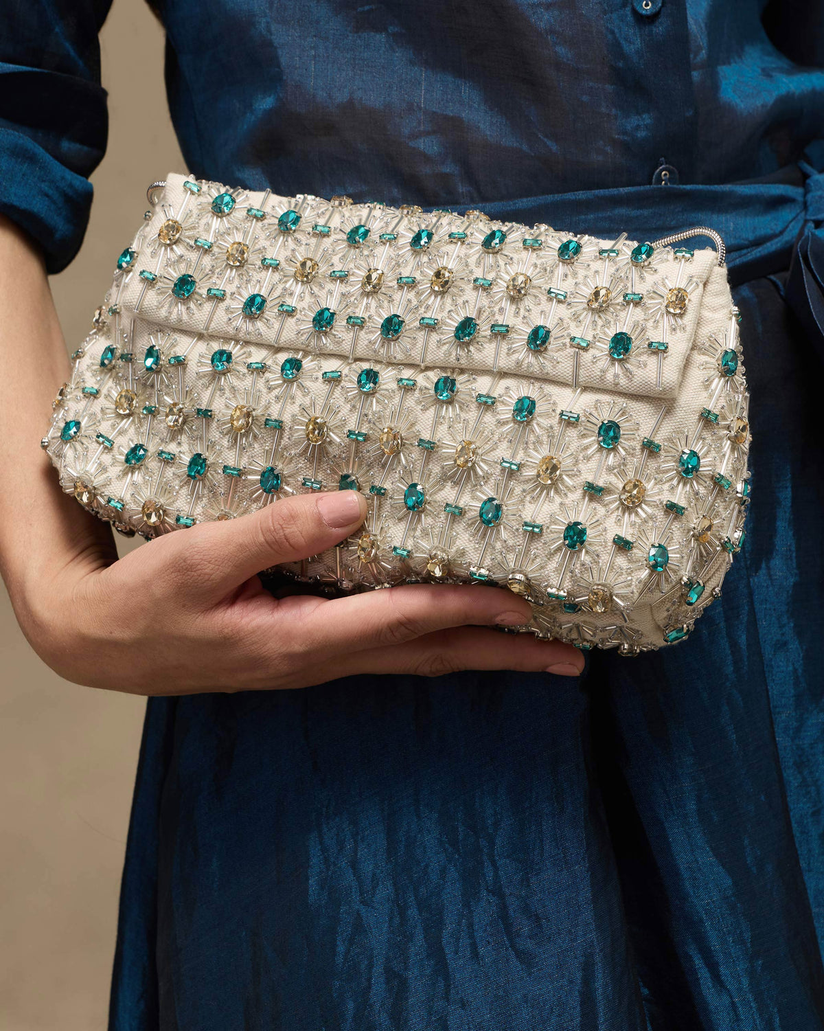 Ivory Noor Clutch with teal gem beadwork held against a teal dress.