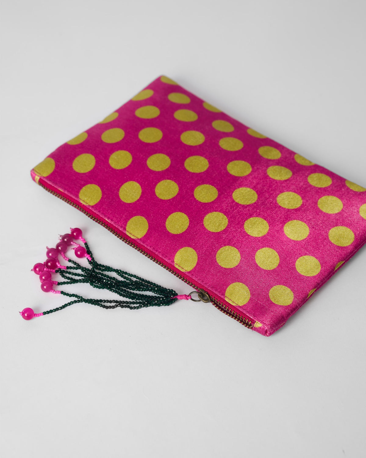 Fuchsia pouch with lime polka dots laid flat, showing zipper and beaded tassel.