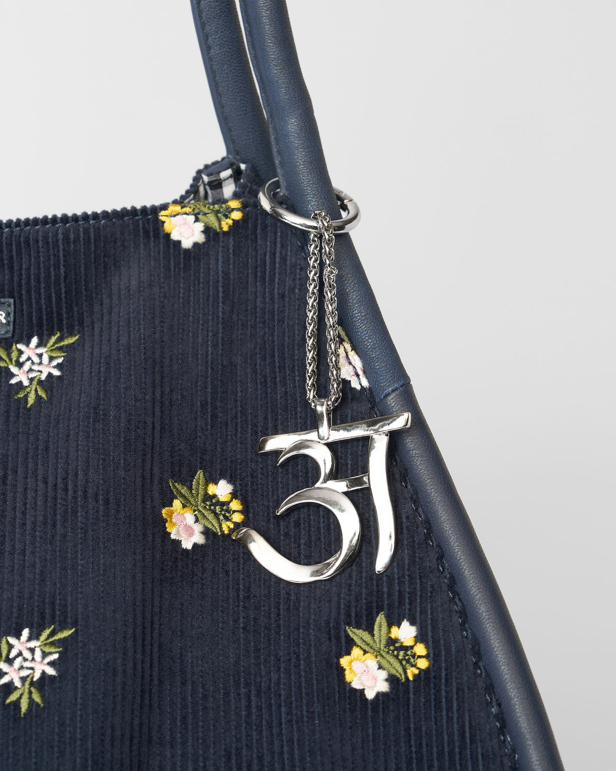 Alphabet A Bag Charm in silver hanging from a navy bag with floral embroidery.
