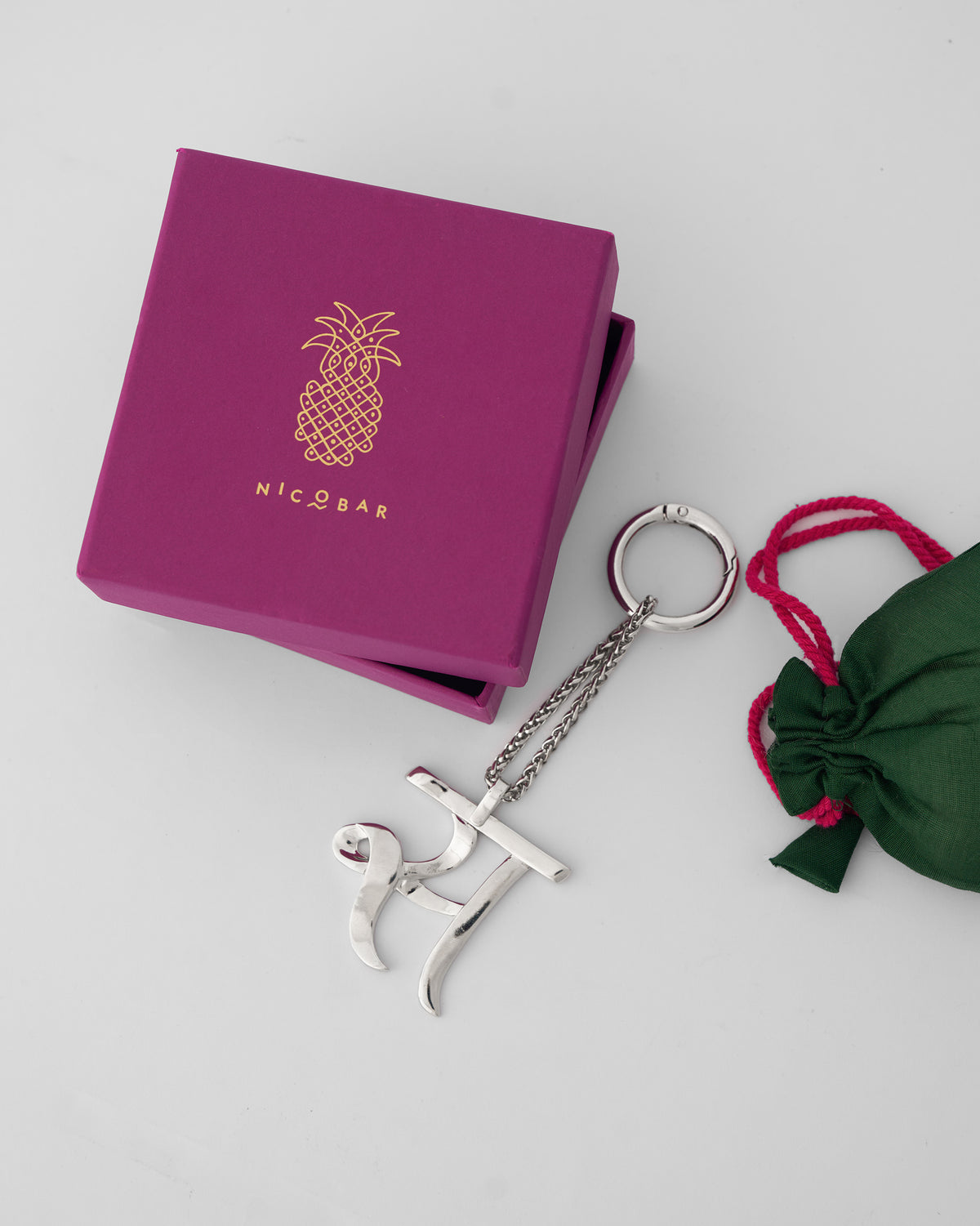 Alphabet S Bag Charm in silver beside a magenta Nicobar gift box and green pouch.