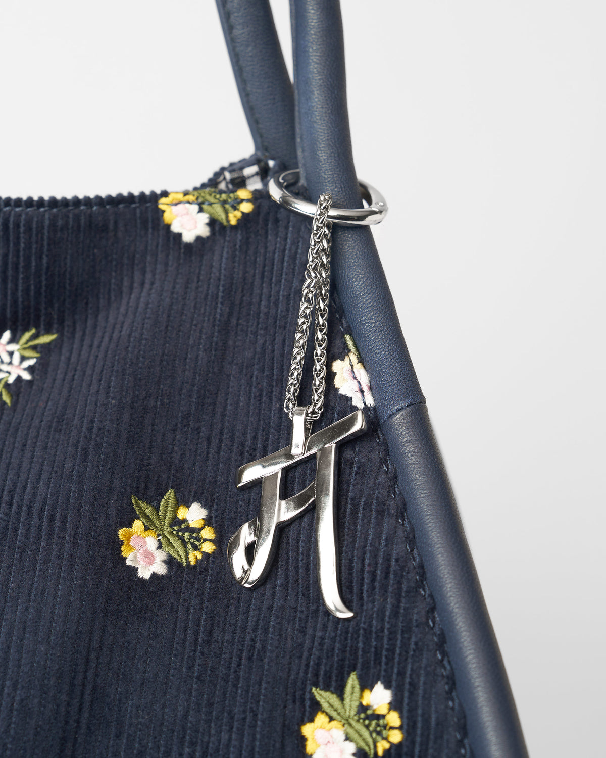 Alphabet M Bag Charm in silver hanging from a navy bag with floral embroidery.