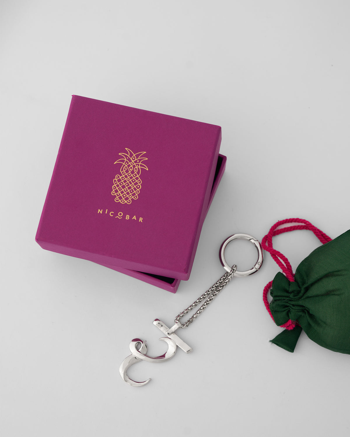 Alphabet R Bag Charm in silver beside a magenta Nicobar gift box and green pouch.