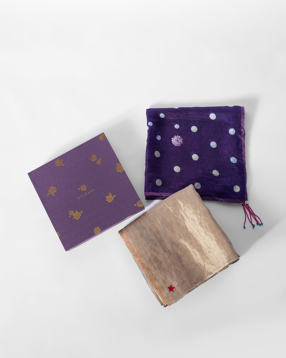 Astral Scarf folded in gold and grey beside a purple gift box.