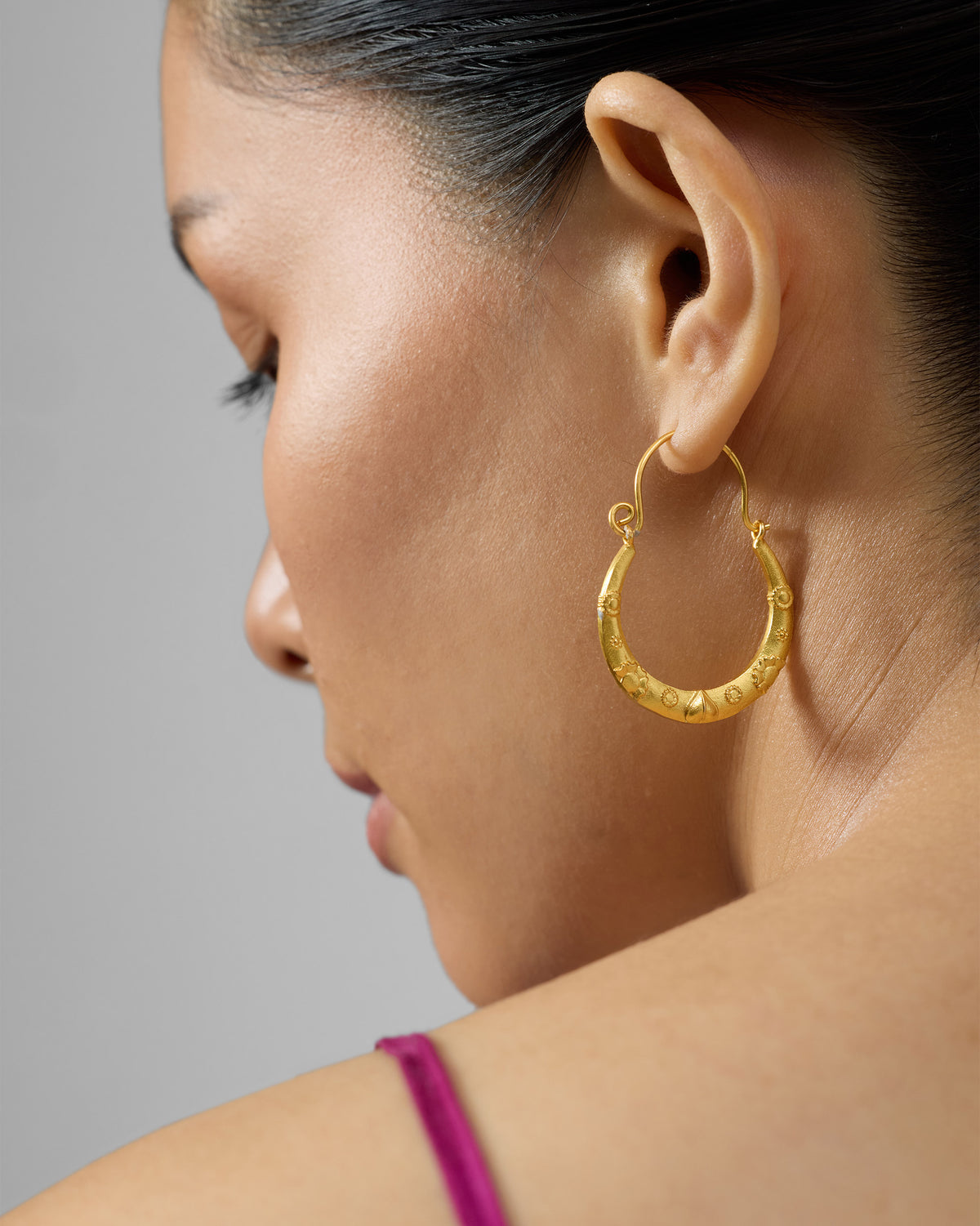 Side profile of gold ellora balis with embossed floral motifs.