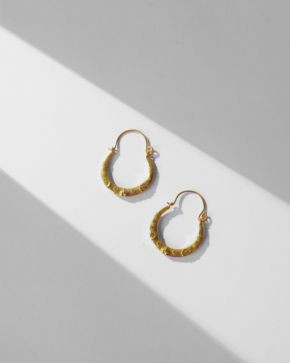 Pair of gold ellora balis with embossed motifs laid flat.