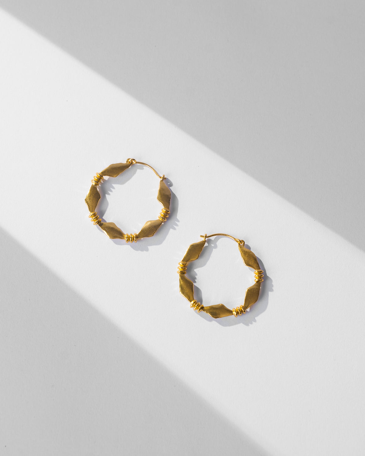 Pair of gold Pillar balis with geometric segments laid flat.